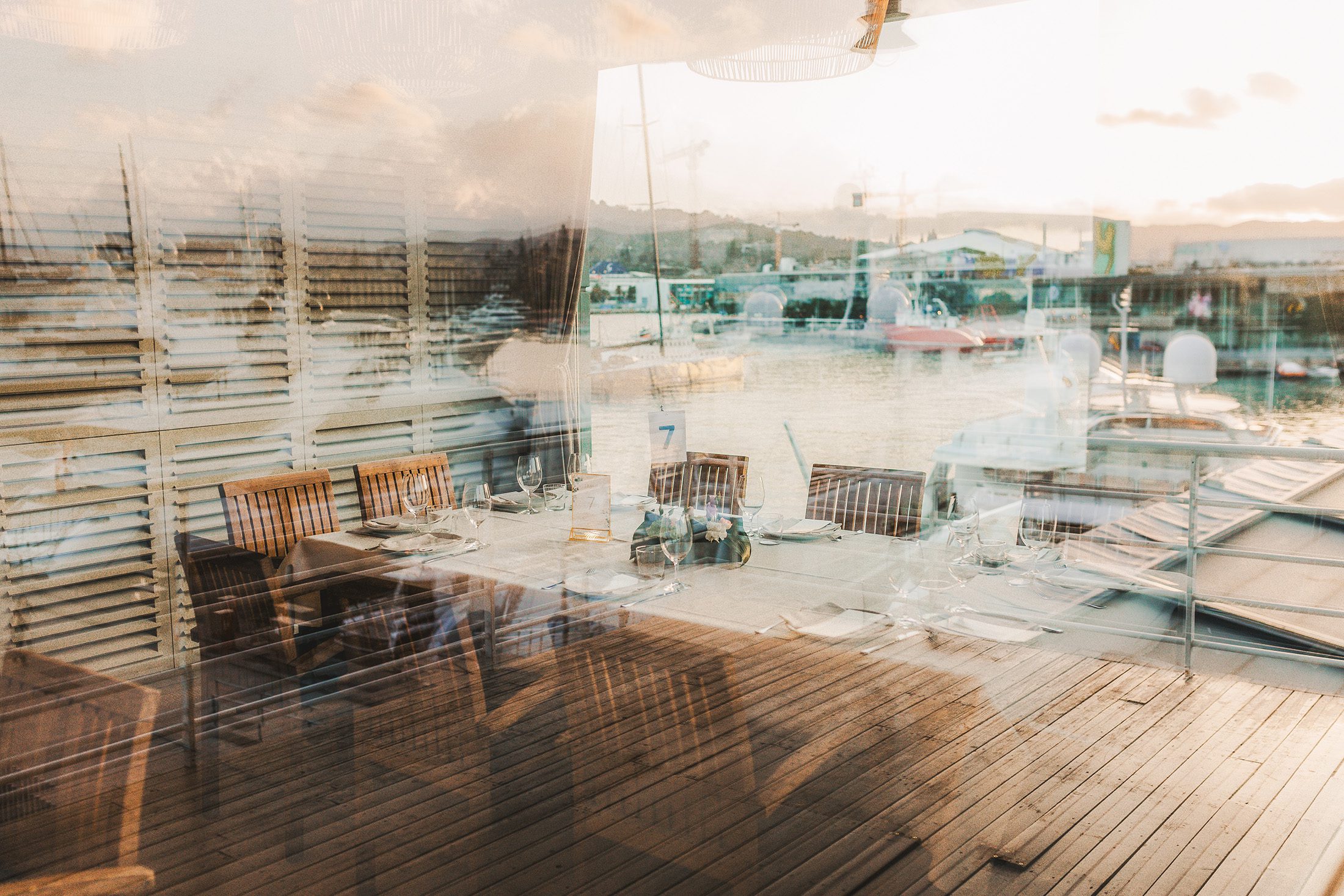 Reflection of a waterfront restaurant terrace in Barceloneta, Barcelona, overlooking the marina at sunset.