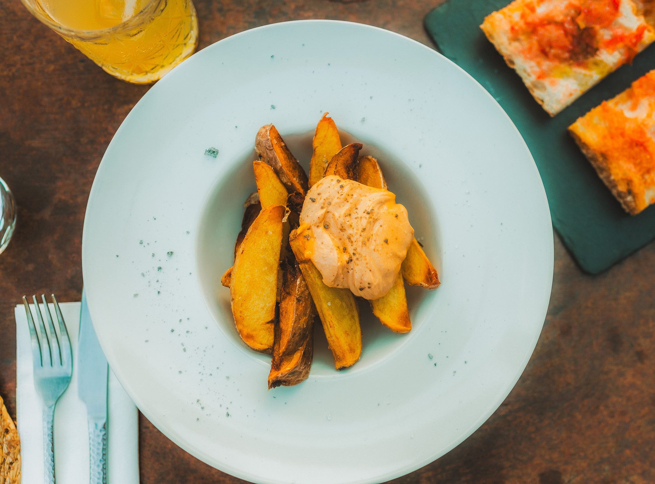 Overhead food photography of crispy potato wedges served with creamy aioli at a Mediterranean restaurant.