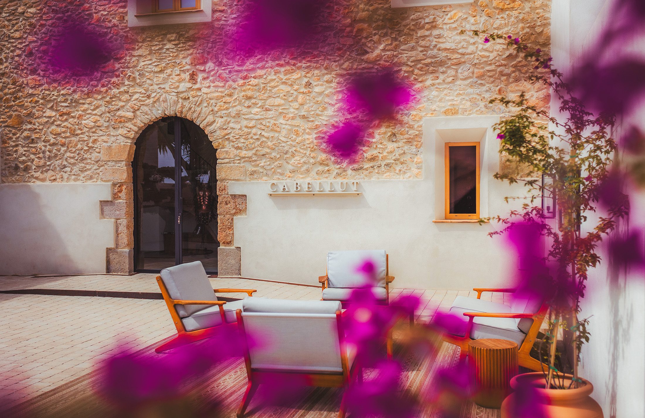 Elegant courtyard lounge at Masia Cabellut vineyard estate in Tarragona framed by vibrant bougainvillea flowers and Mediterranean architecture.
